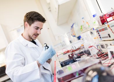 Zu sehen ist ein Mann in einem Labor, beim Experimentieren an einem Labortisch, der voller Instrumente ist.