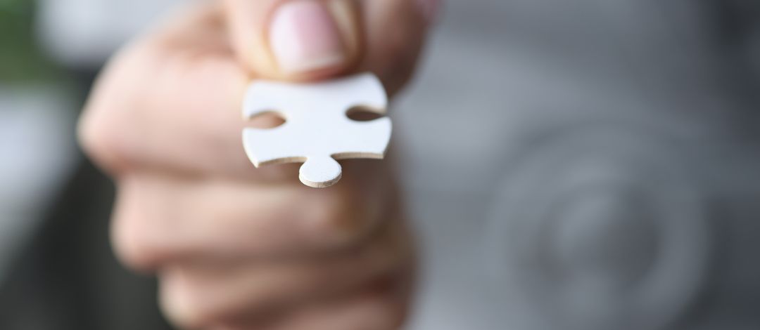 Photo of a hand holding a white puzzle piece.