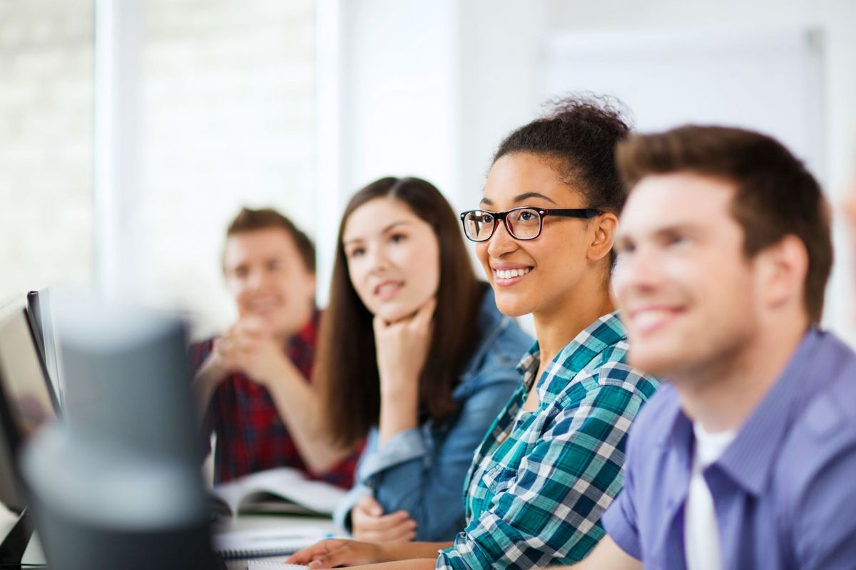 enlarge the image: Vier Studierende sitzen an PCs und hören Aufmerksam einer Person außerhalb des Bildes zu