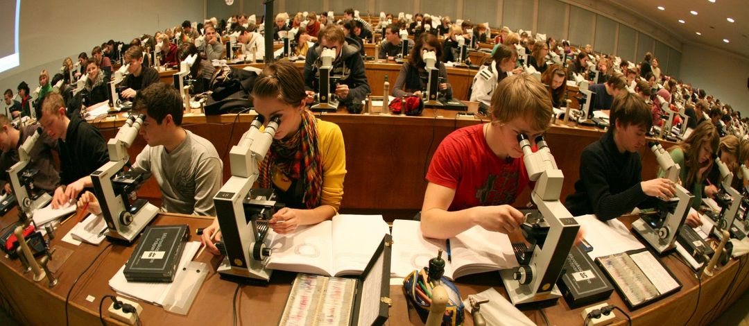 Foto: Studierende sitzen in einem vollem Hörsaal an den Mikroskopen und arbeiten 