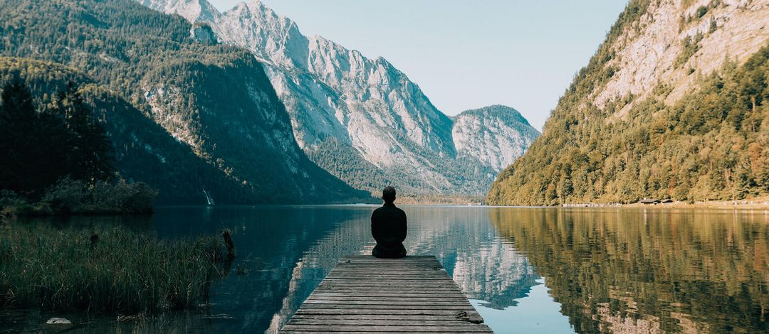 Ein Mann meditiert vor einem Bergsee