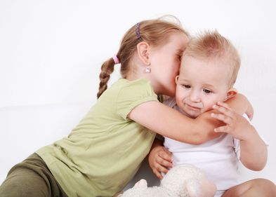 Auf dem Bild ist ein kleiner Junge zu sehen, der von seiner älteren Schwester umarmt wird.
