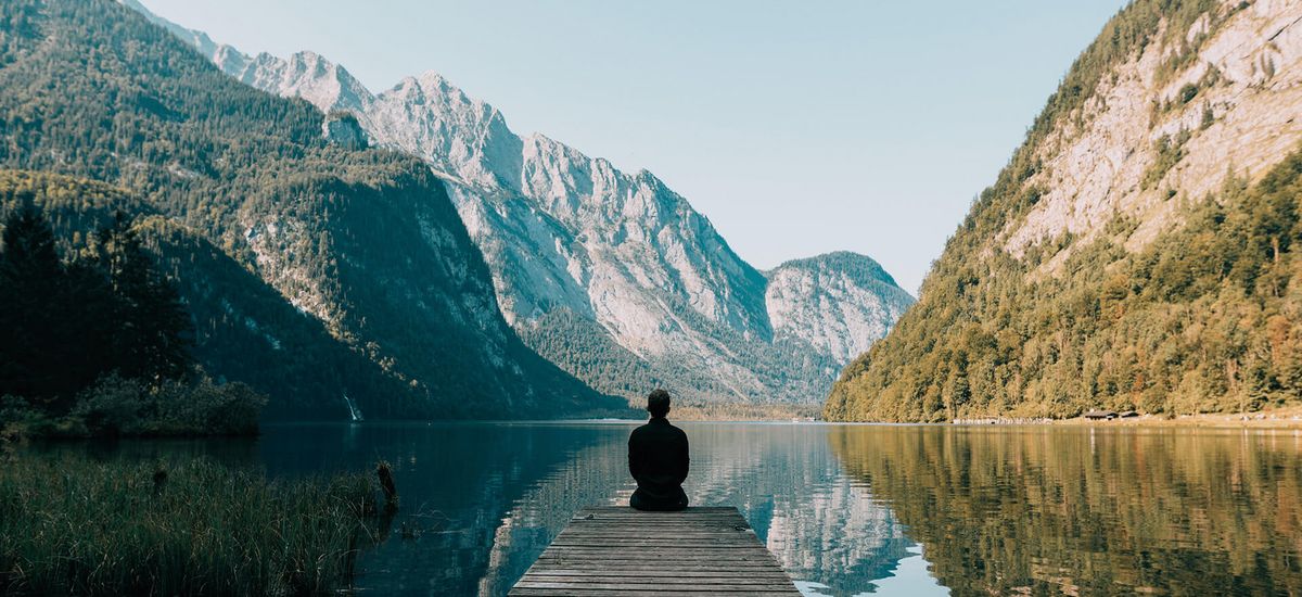 Ein Mann meditiert vor einem Bergsee