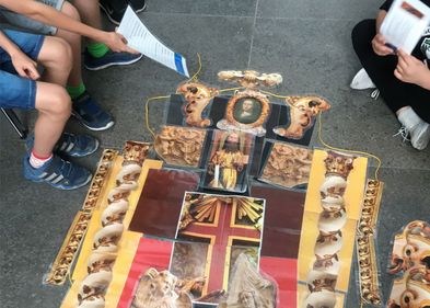 Das museumspädagogische Zentrum Forum Take 5 in der Strohsackpassage bietet zur Museumsnacht verschiedene Kreativangebote an, Foto: Christine Hübner/Kustodie Farbfoto: auf dem Boden liegen einzelne Bilder eines Epitaphs, die wie ein Puzzle zu einem Gesamtbild zusammengesetzt sind. Um das Puzzel sind einzelne Kinderbeine zu sehen, die auf Stühlen um das Kunstwerk sitzen.