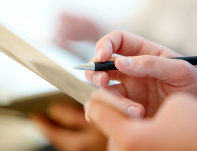 Hände einer Person halten einen Zettel und einen Stift, um Notizen zu machen.