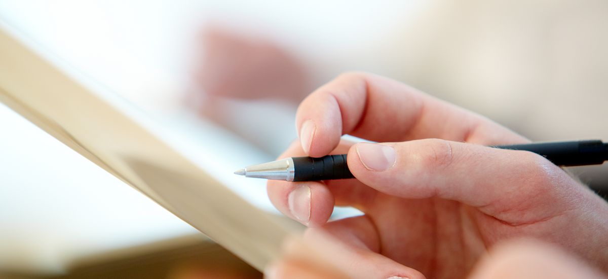 Hände einer Person halten einen Zettel und einen Stift, um Notizen zu machen.
