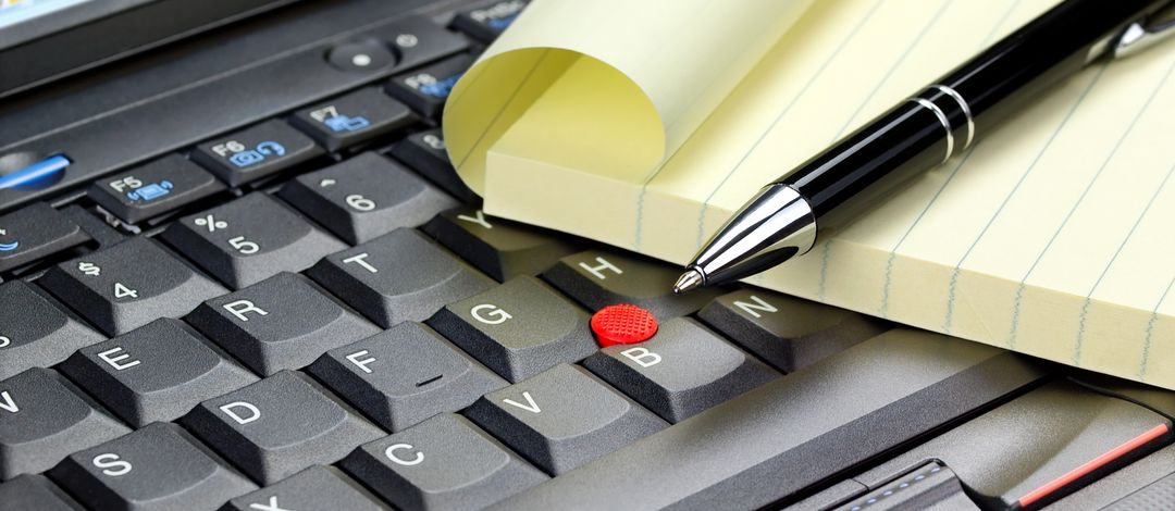 The picture shows a laptop keyboard with a pad and a pen on it. 