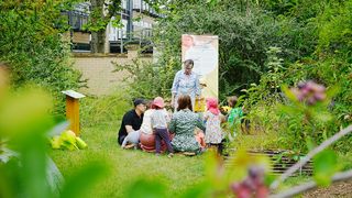 Die Projektleiterin des Projektes Kindergarten - Gartenkinder erklärt einer Gruppe Kinder das Programm und den Ablauf des Tages. Die Kinder sitzen im Kreis. Foto: Dorett Bothmann