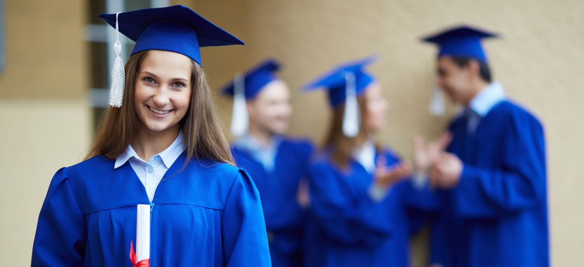 Bild zeigt eine Frau im Vordergrund mit einem Diplom in der Hand und drei Personen im Hintergrund, die miteinander sprechen. Alle tragen blaue traditionelle Abschlussroben