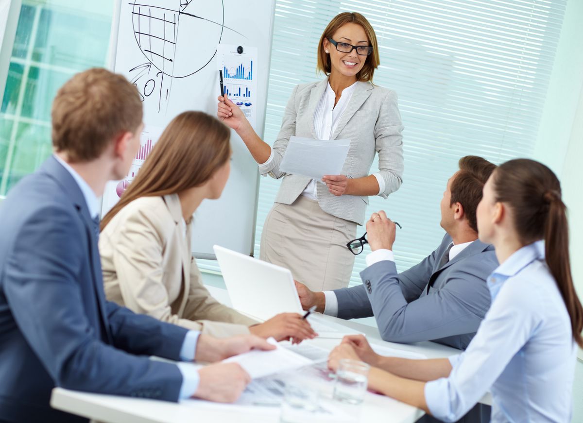 enlarge the image: Bild zeigt fünf Personen; Vier schauen zu einer Frau, welche etwas auf einem Whiteboard zeigt und erklärt